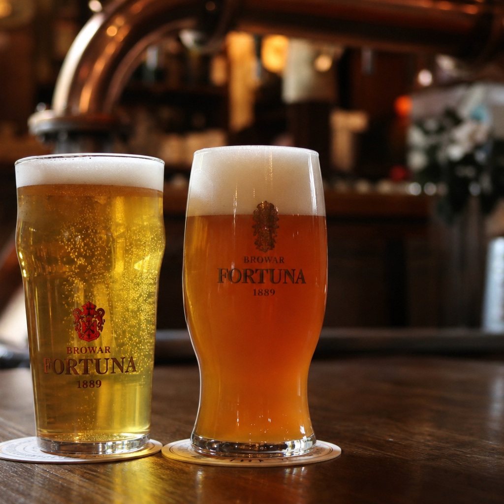 Zwei Biergläser auf einem Tisch (ein helles Lager und ein trübes, bernsteinfarbenes Bier) vor verwischtem Hintergrund in warmem Licht